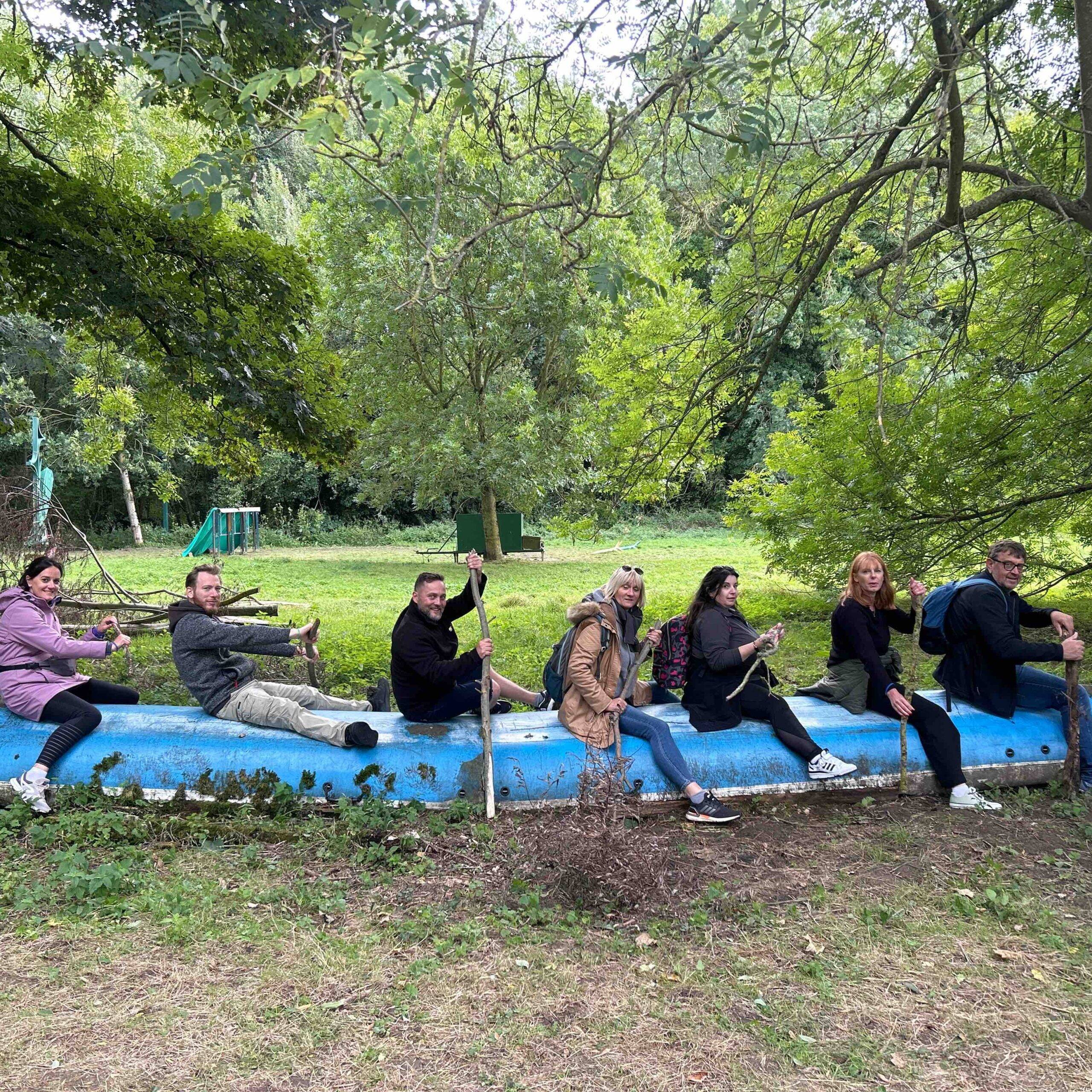 Photo d'une équipe lors d'un team building à Lille qui fait semblant de ramer sur une barque dans l'herbe