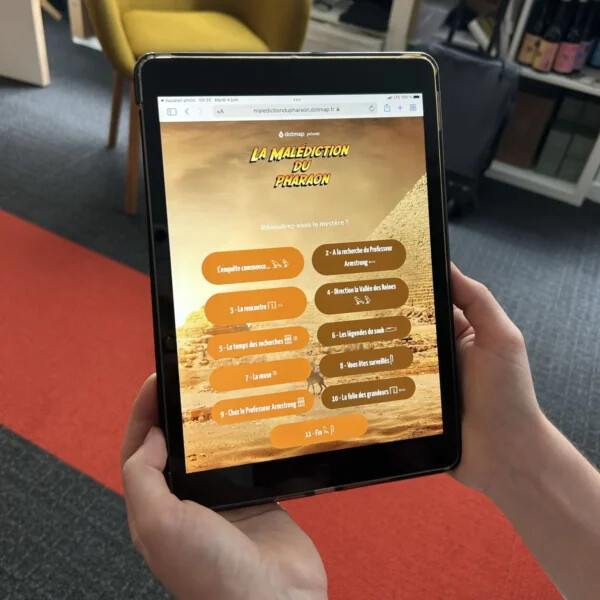 Participante tenant dans les mains un iPad de jeu connecté à la Malédiction du Pharaon, une enquête collaborative